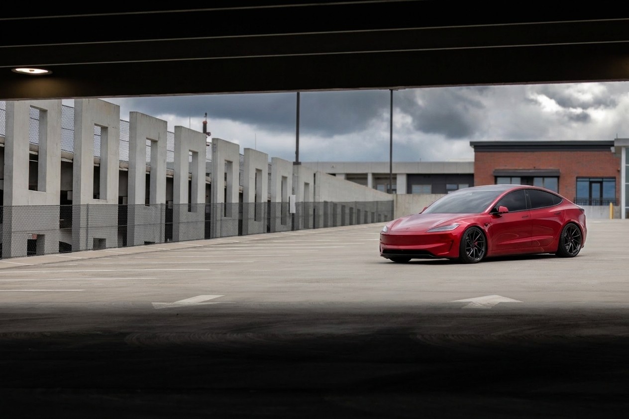 Red Tesla Model 3 Performance on rooftop parking deck under overcast sky